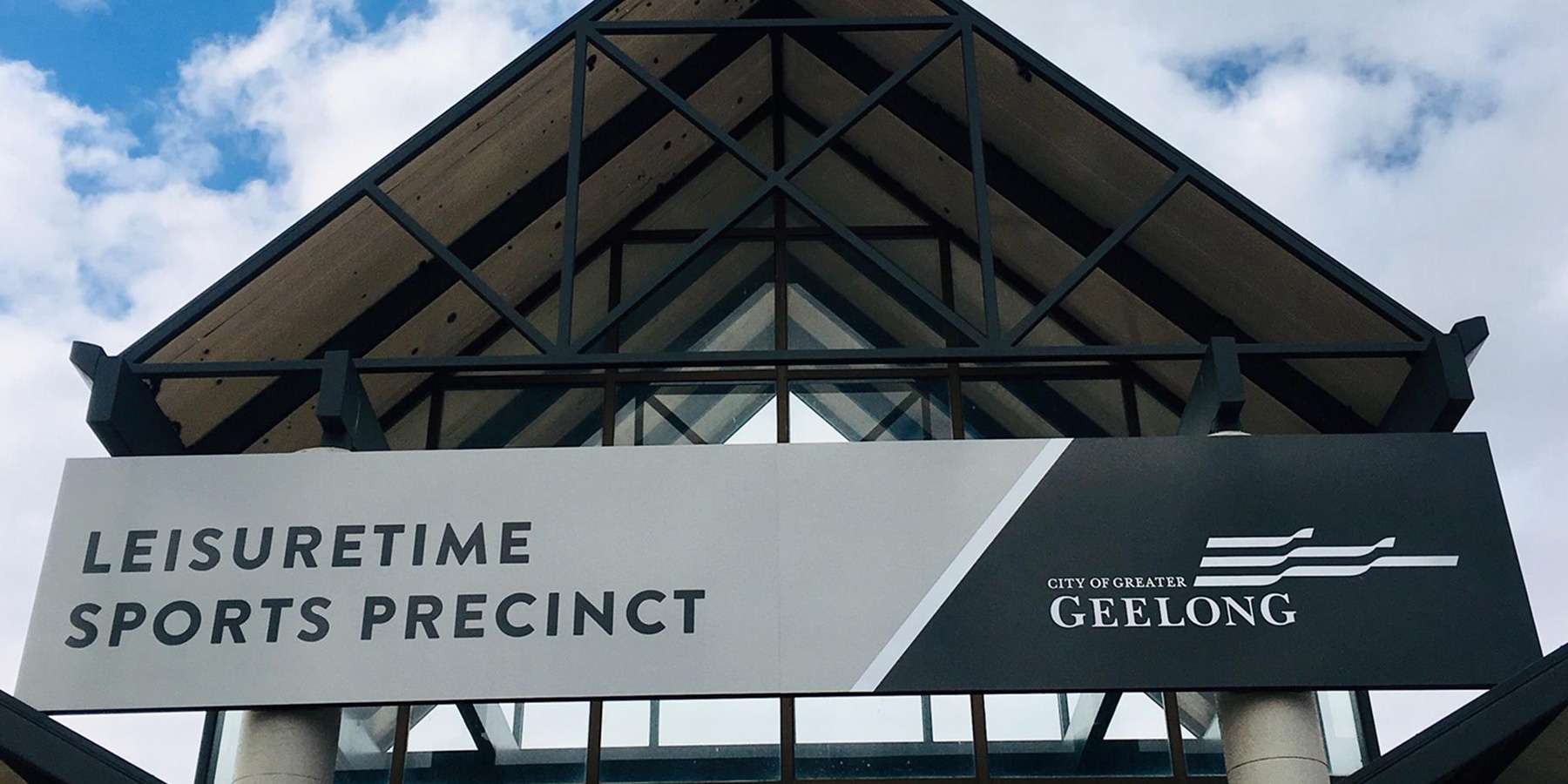 Signage for Leisuretime Sports Precinct, Geelong, displayed under a modern building structure against a cloudy sky.