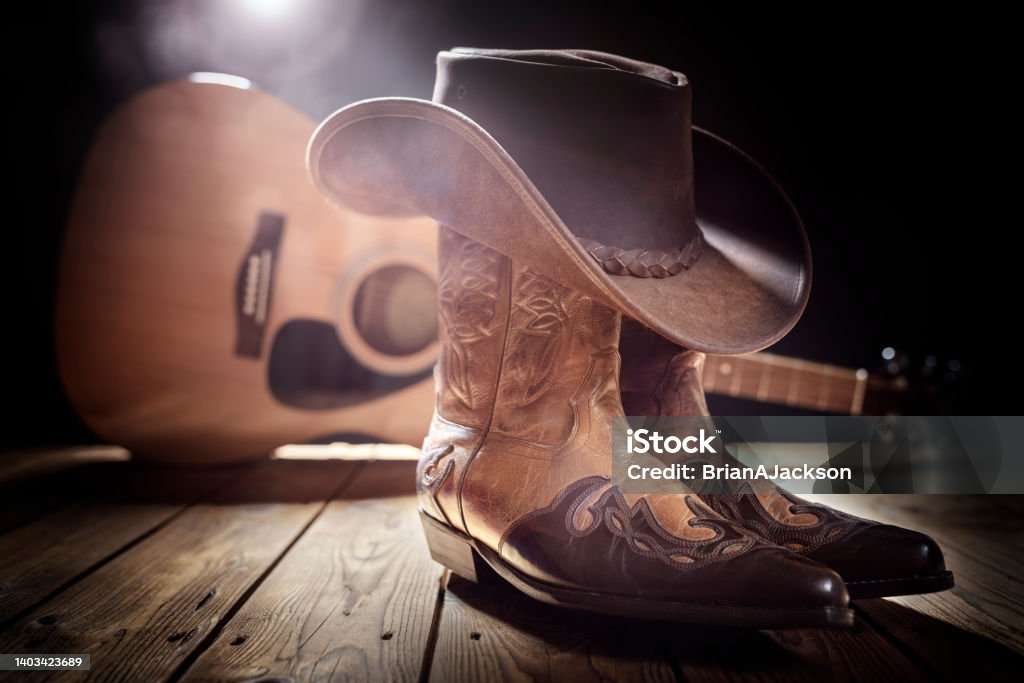 Photo of guitar behind a poor of line dancing boots with a cowboy hat balanced on top of the boots