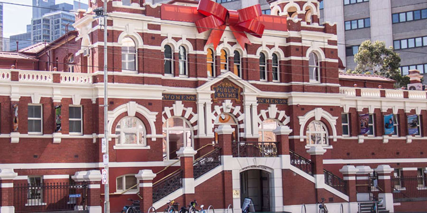 Historic red brick building adorned with a large red bow, symbolizing festive decorations amid a city skyline.
