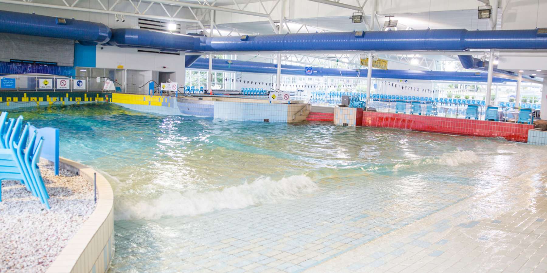 Indoor wave pool with gentle waves, colorful barriers, and lounge chairs, creating a fun and relaxed aquatic environment.