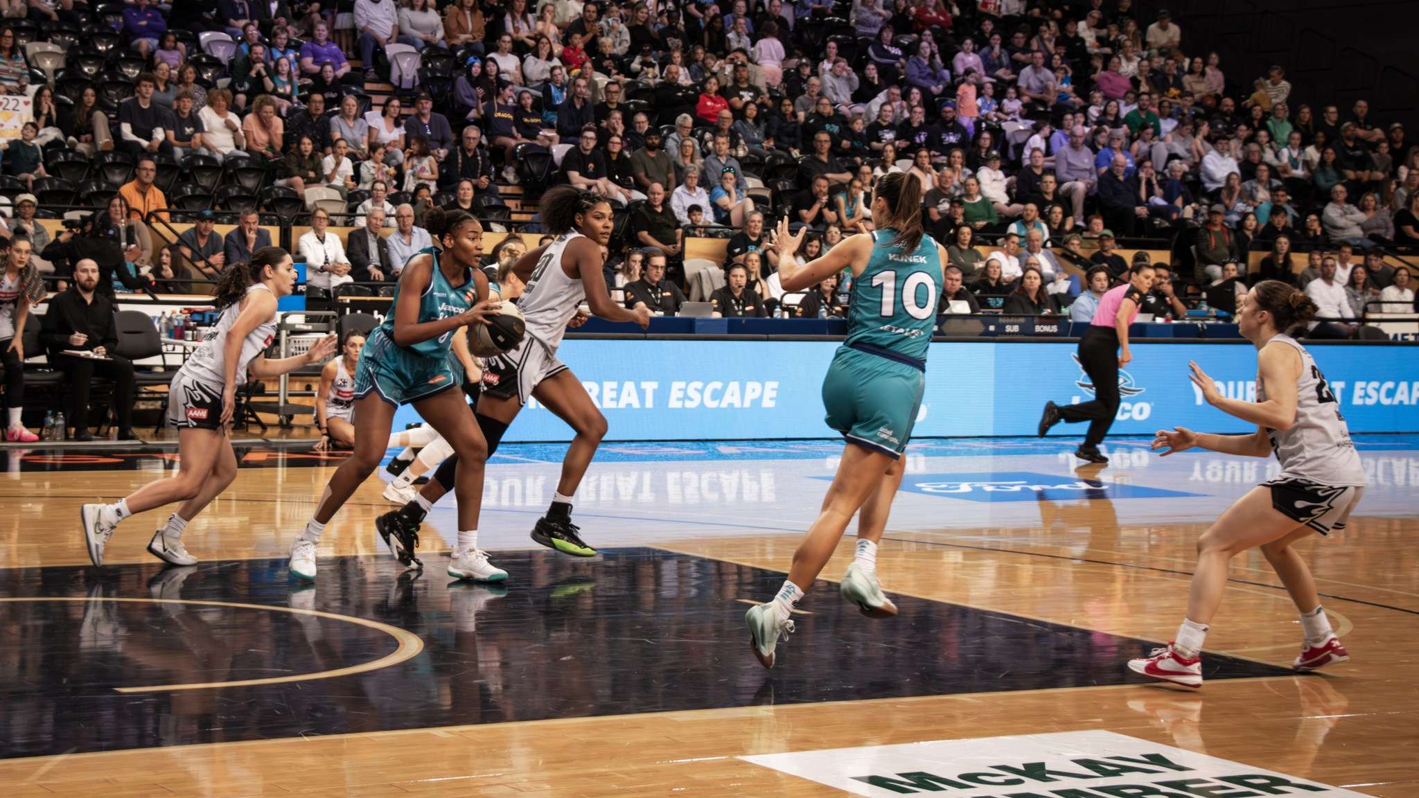 A large indoor basketball court with grandstand and female basketball players playing a basketball game.