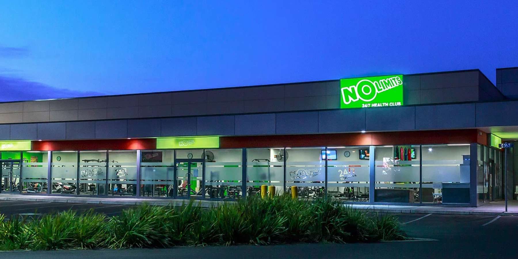 Exterior of a retail store at dusk, featuring a bright green "NO" sign and illuminated windows.