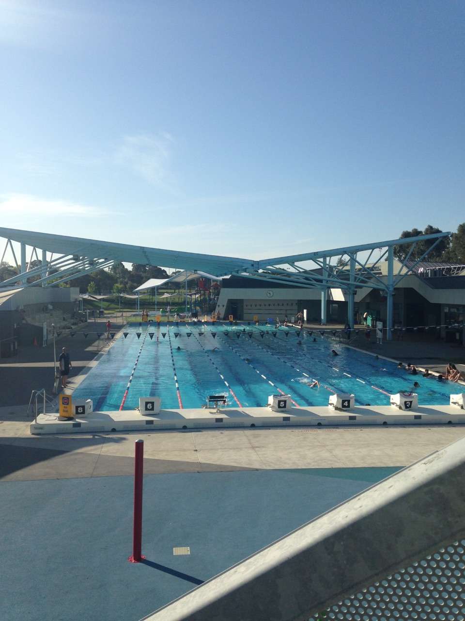 An indoor inground level swimming pool with multiple lanes divided by ropes with multi coloured shade sails above.