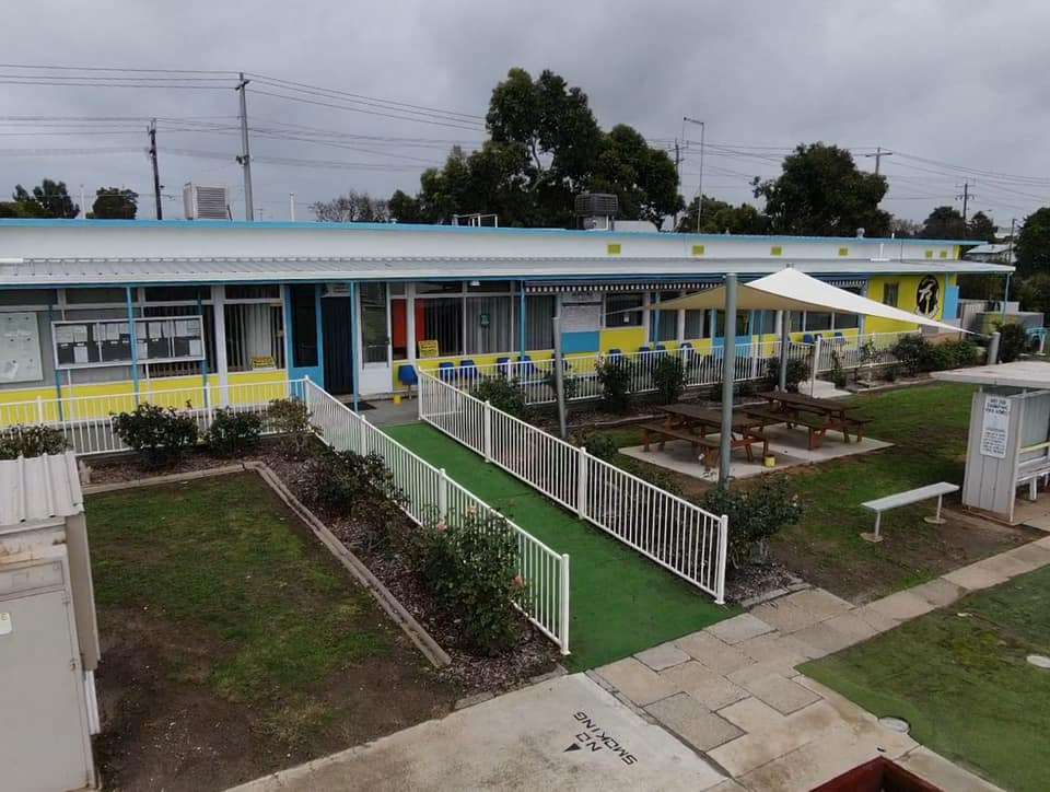 A white building with a green grassed entry with tables and sunshades.