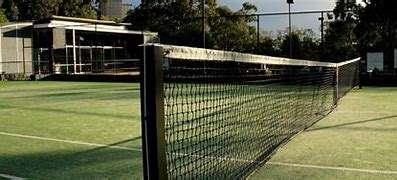 A tennis court with a net in the foreground, featuring a well-maintained green surface and a modern building in the background.