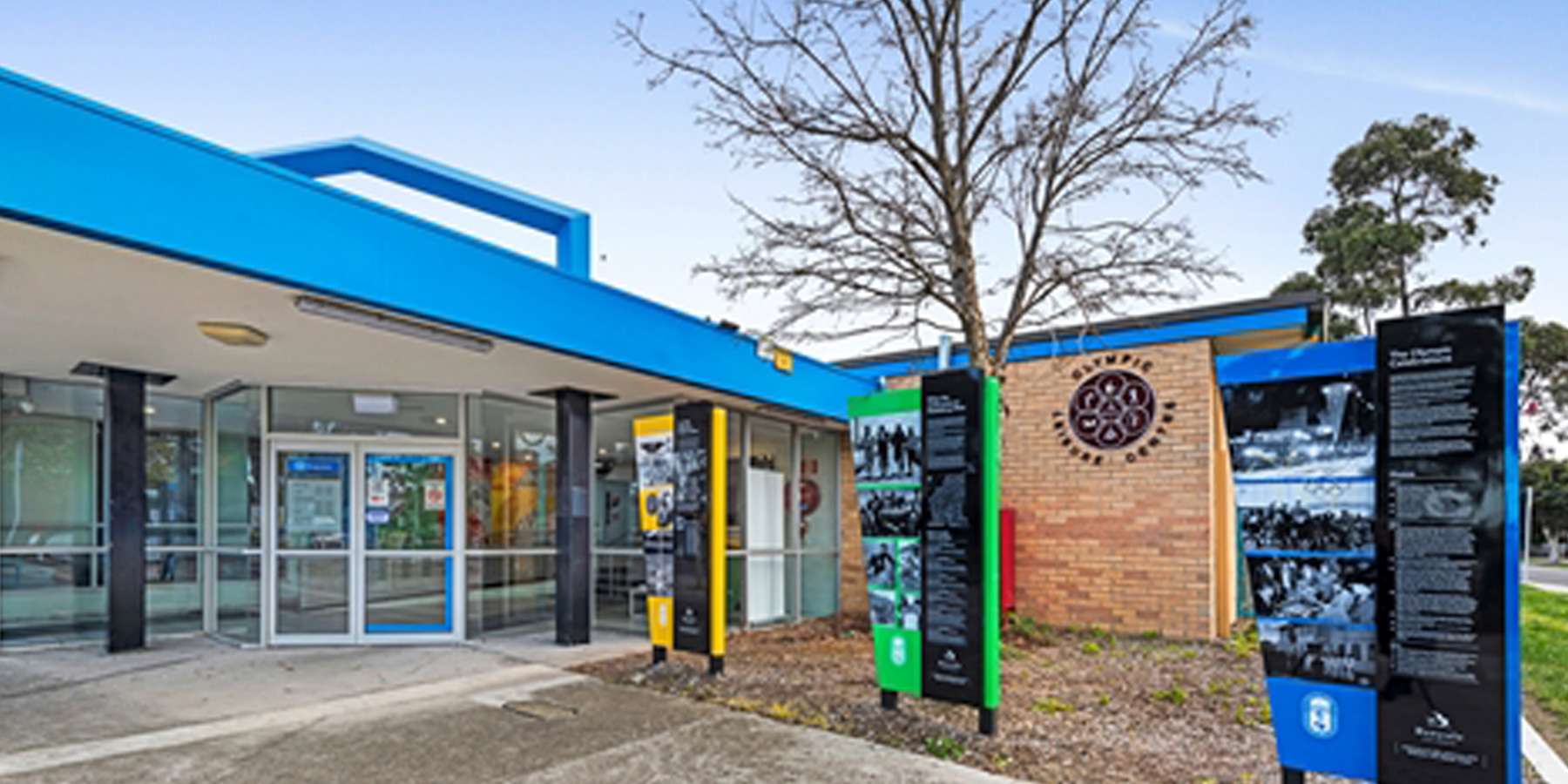 Modern building entrance with colorful signage, surrounded by trees, showcasing a welcoming community center or educational facility.