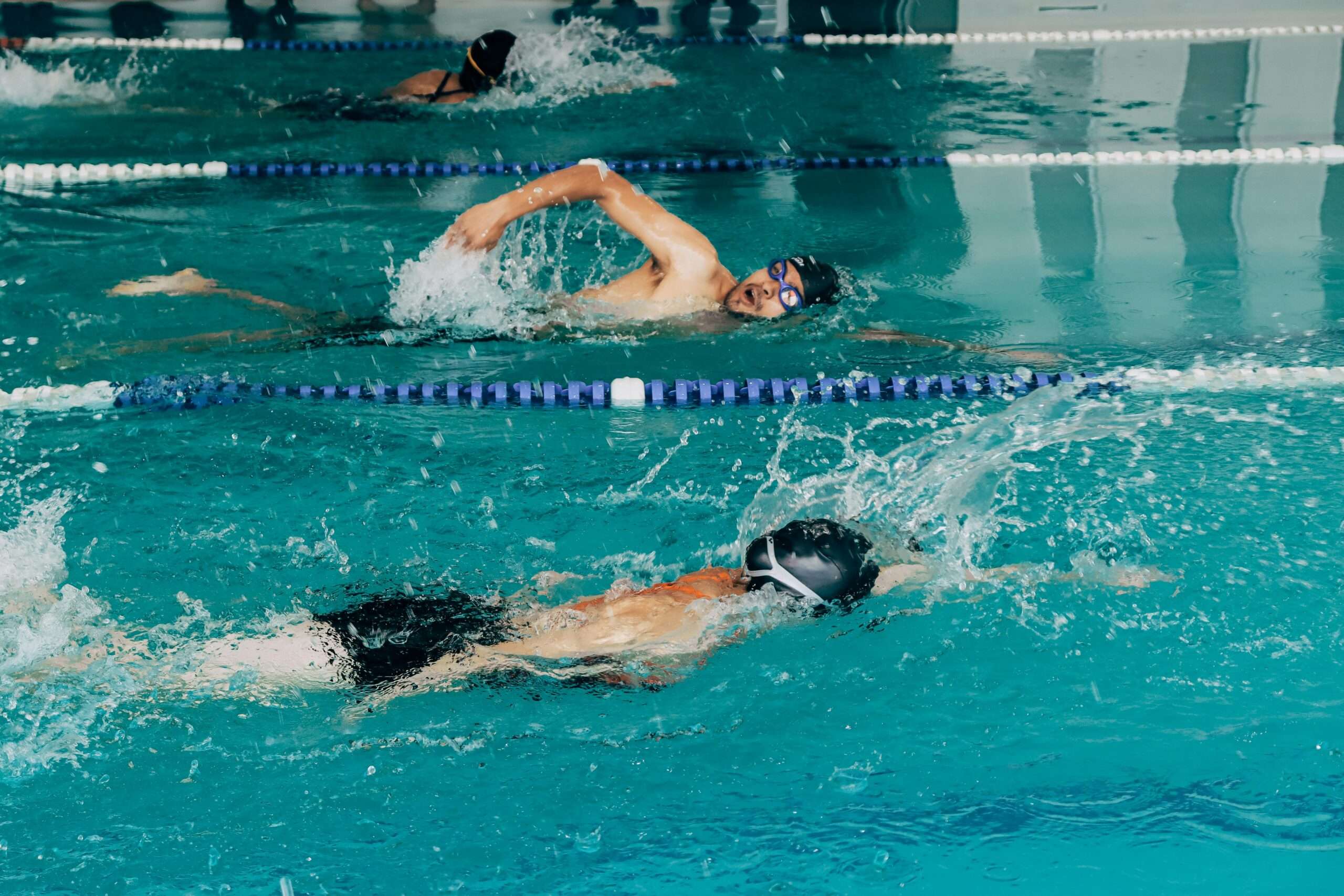 Two swimmers compete in a pool, one performing freestyle and the other backstroke, creating splashes in the water.