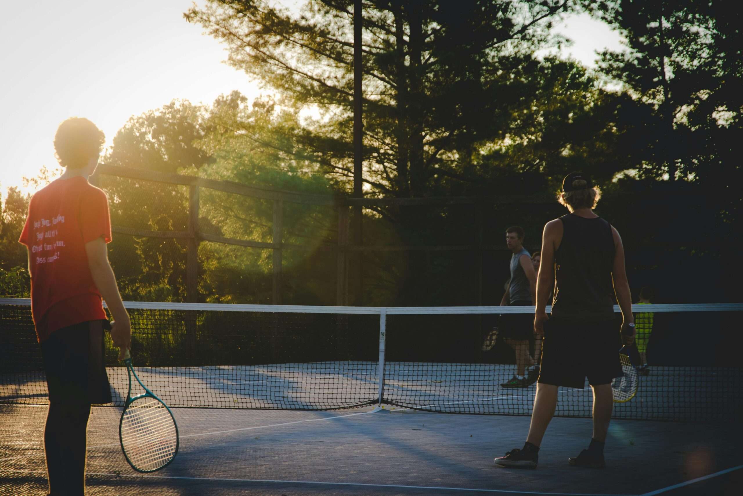 two people standing at a tennis net with racquets in the sunset