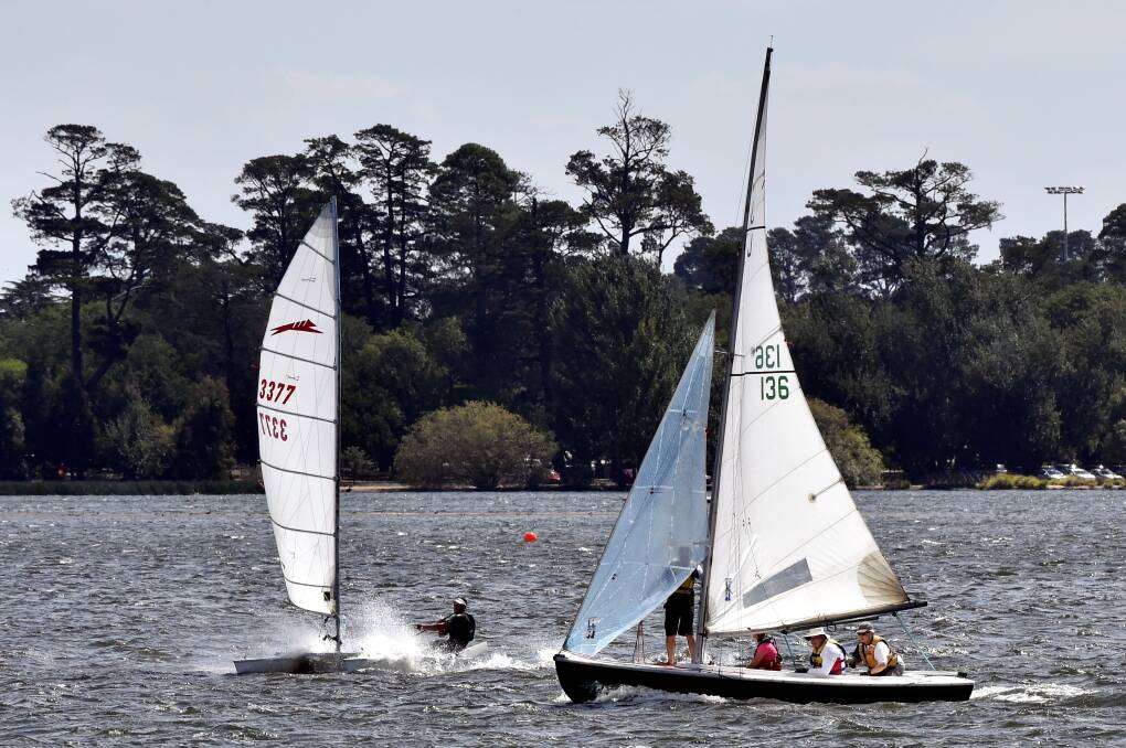 Two sailboats glide across a shimmering body of water, surrounded by lush trees under a clear blue sky.