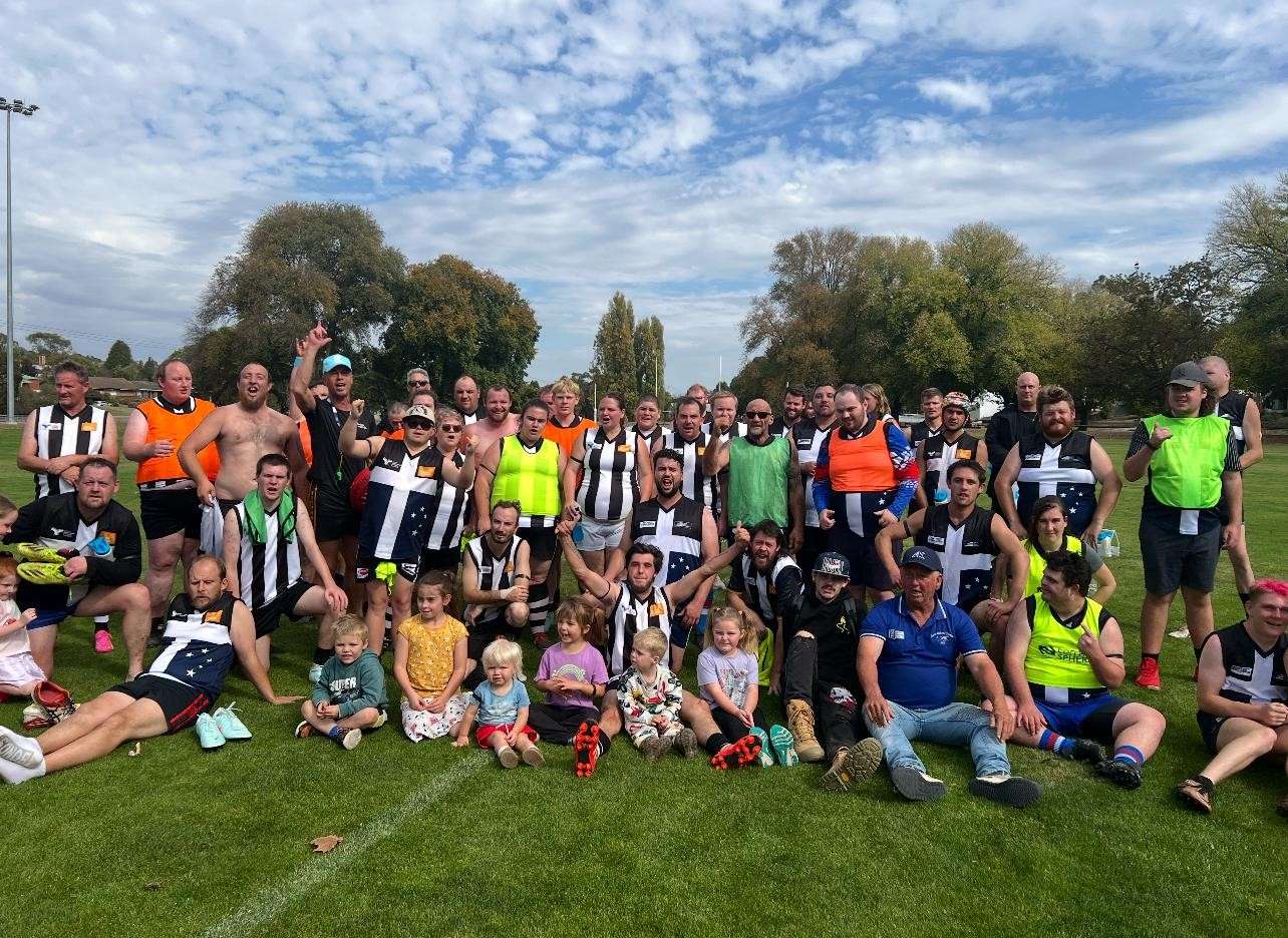 A large group of people wearing team jerseys and colored vests poses on a grassy field