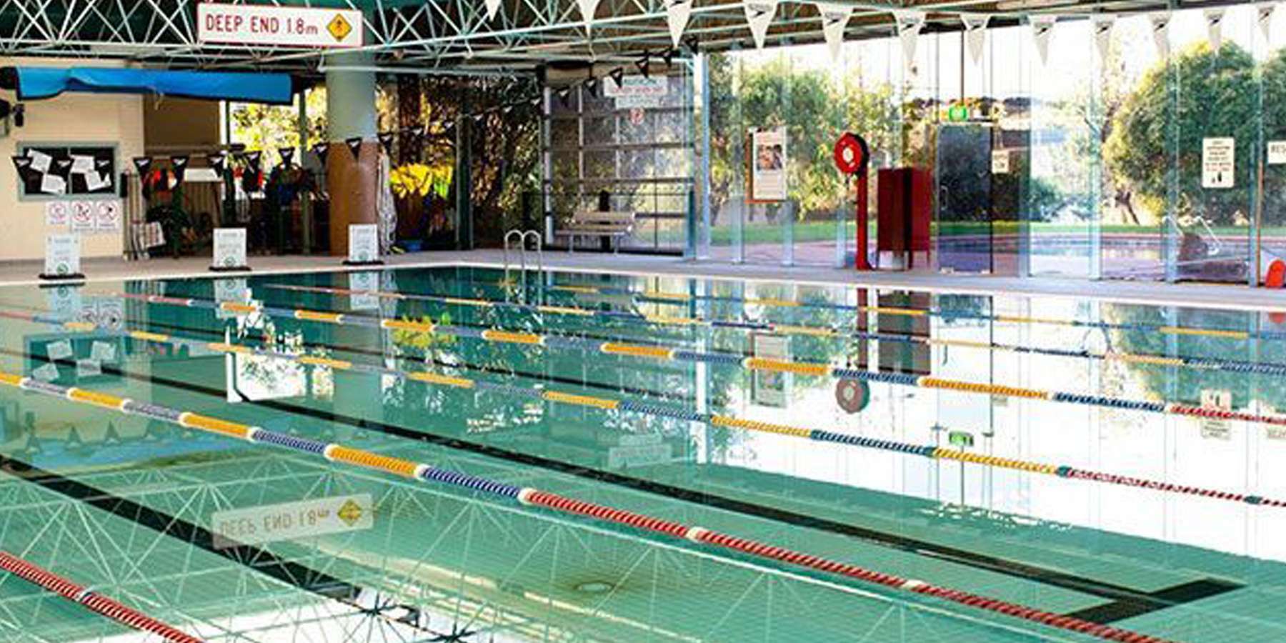 Indoor swimming pool with clear water and marked lanes, featuring a lifeguard station and large windows for natural light.