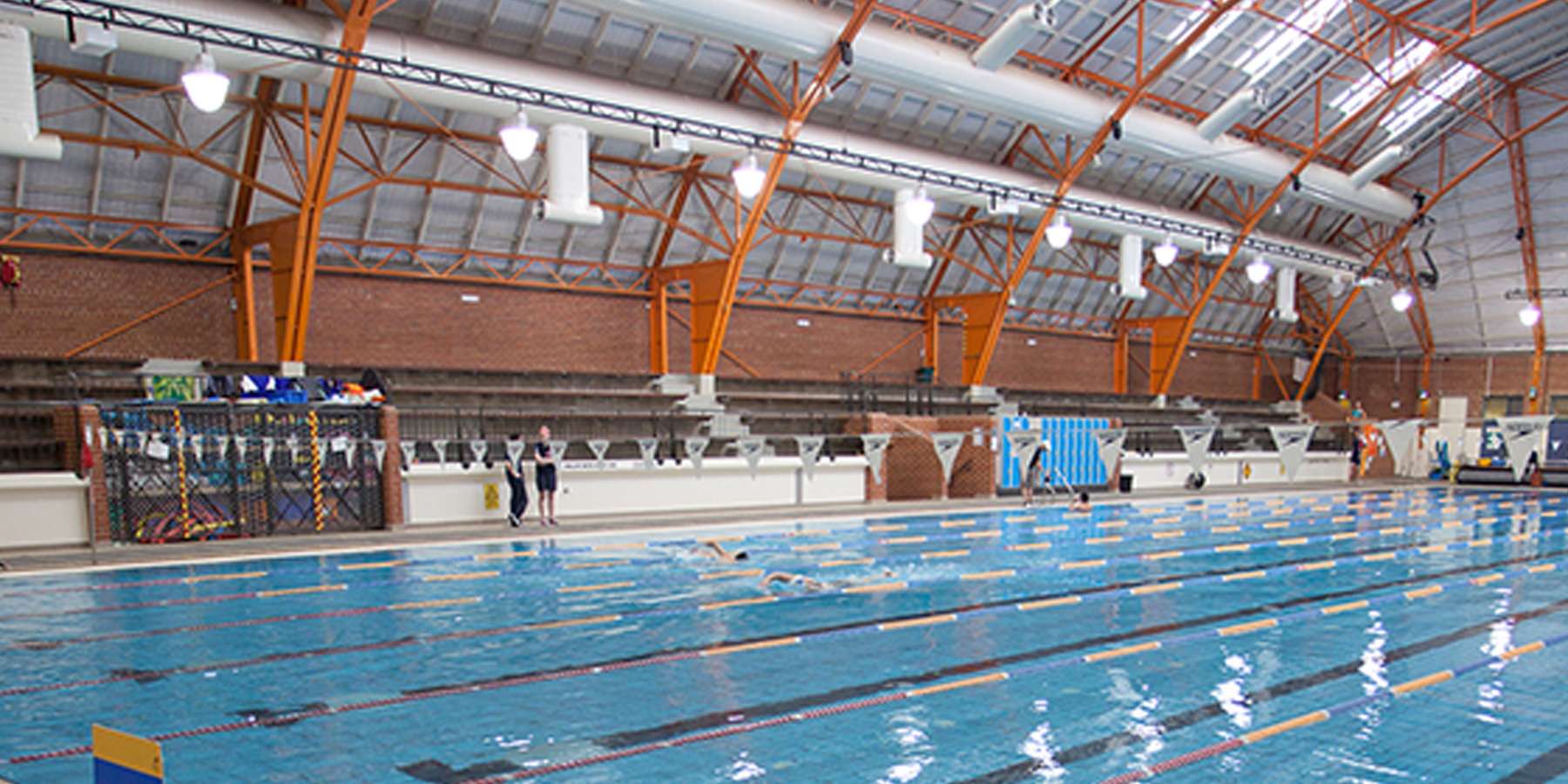 Indoor swimming pool with blue water, high ceilings, and bright lighting; viewing area with benches in the background.