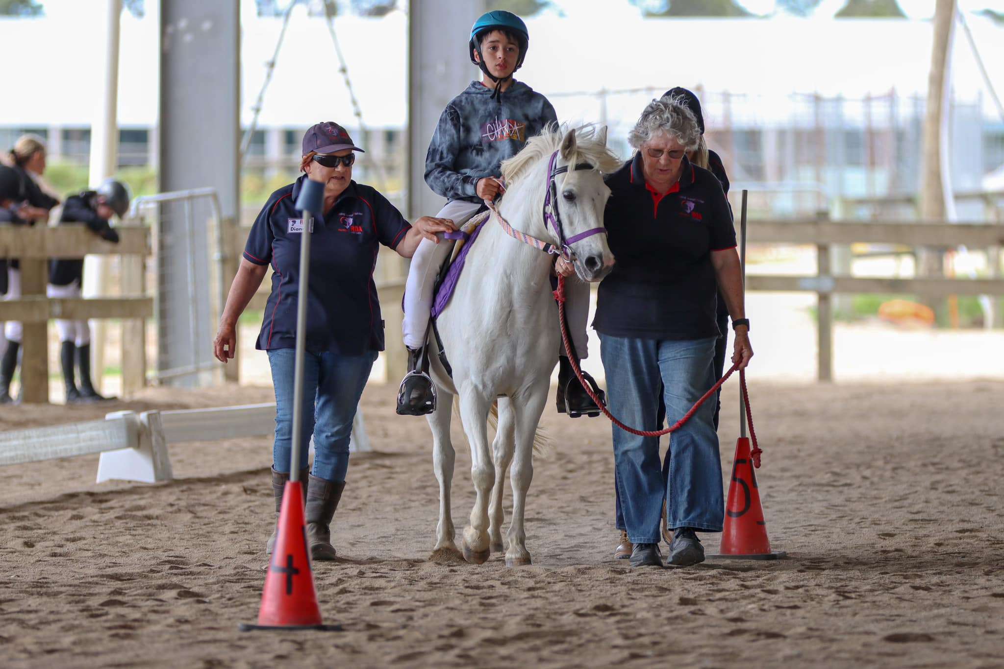 A young boy on a white horse with coaches walking beside.