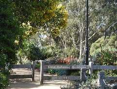 Entrance to Sale Botanic Gardens, featuring a wooden gate framed by lush greenery and colorful flowers.