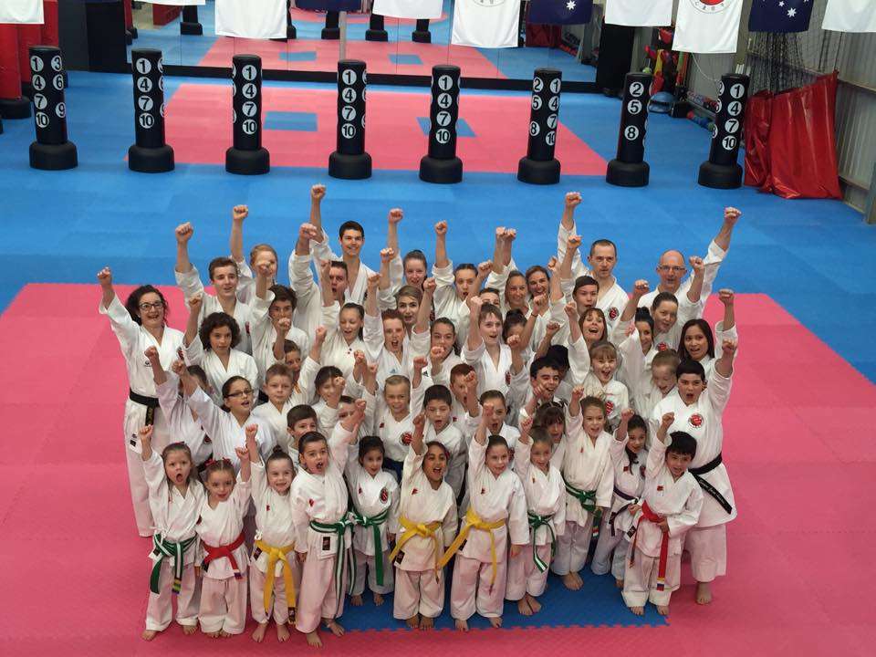 A group of people in karate uniforms with the hands in the air.