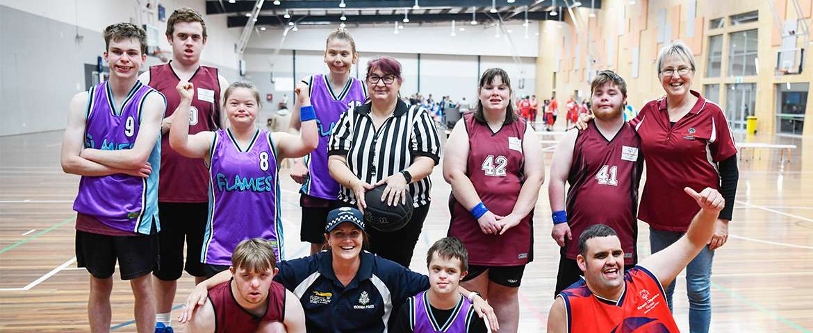 A diverse basketball team poses with their referee in a gym, showcasing team spirit and camaraderie after a game.