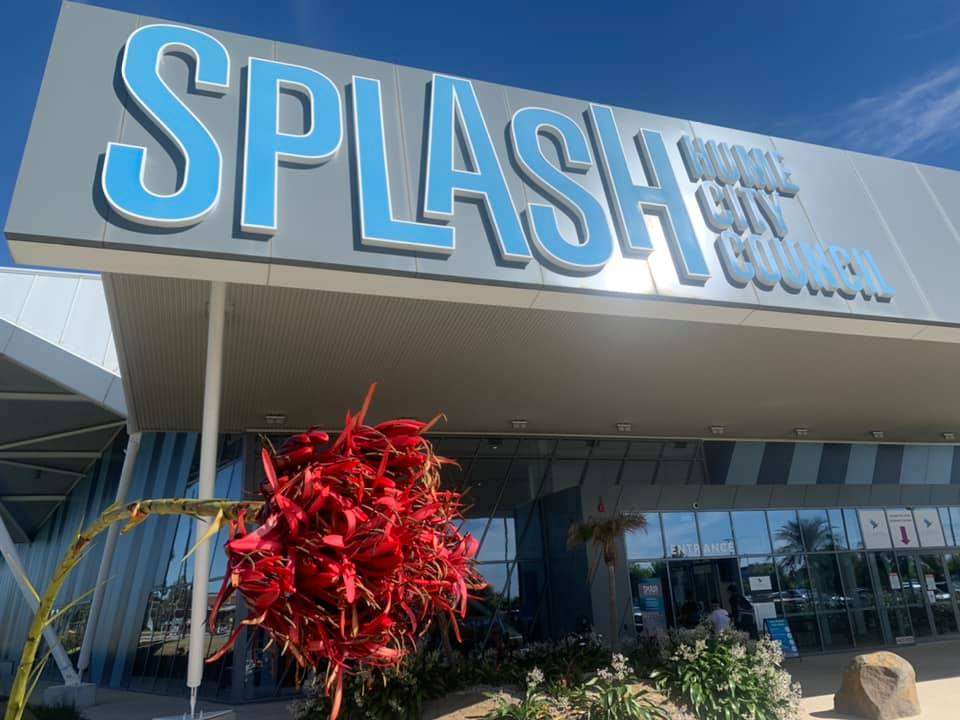 A beige building surrounded by flowers and blue text Splash Hume City Council.