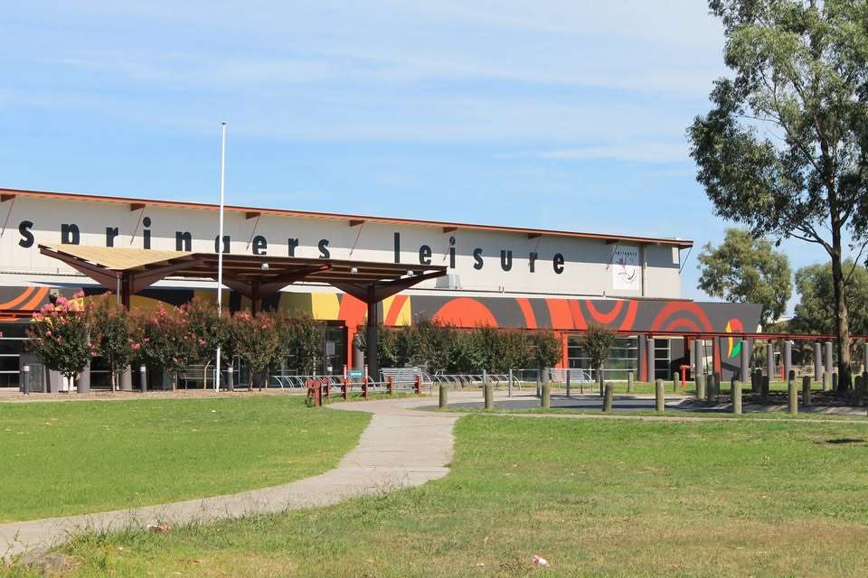 A large white and orange sports stadium surrounded by grass and trees.