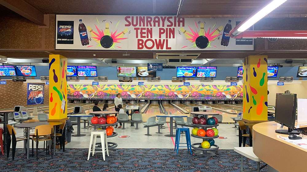 A landscape picture of bowling lanes with bright coloured bowling balls on stands and seating for patrons