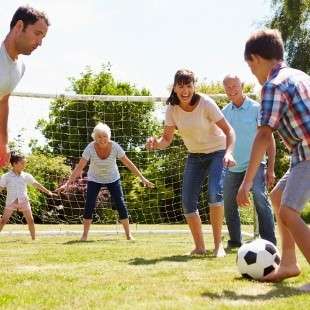A picture of a group of people all different ages playing walking football, there is a soccer ball about to be kicked