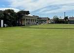Image displays a green flat croquet club, with a building far in the background.