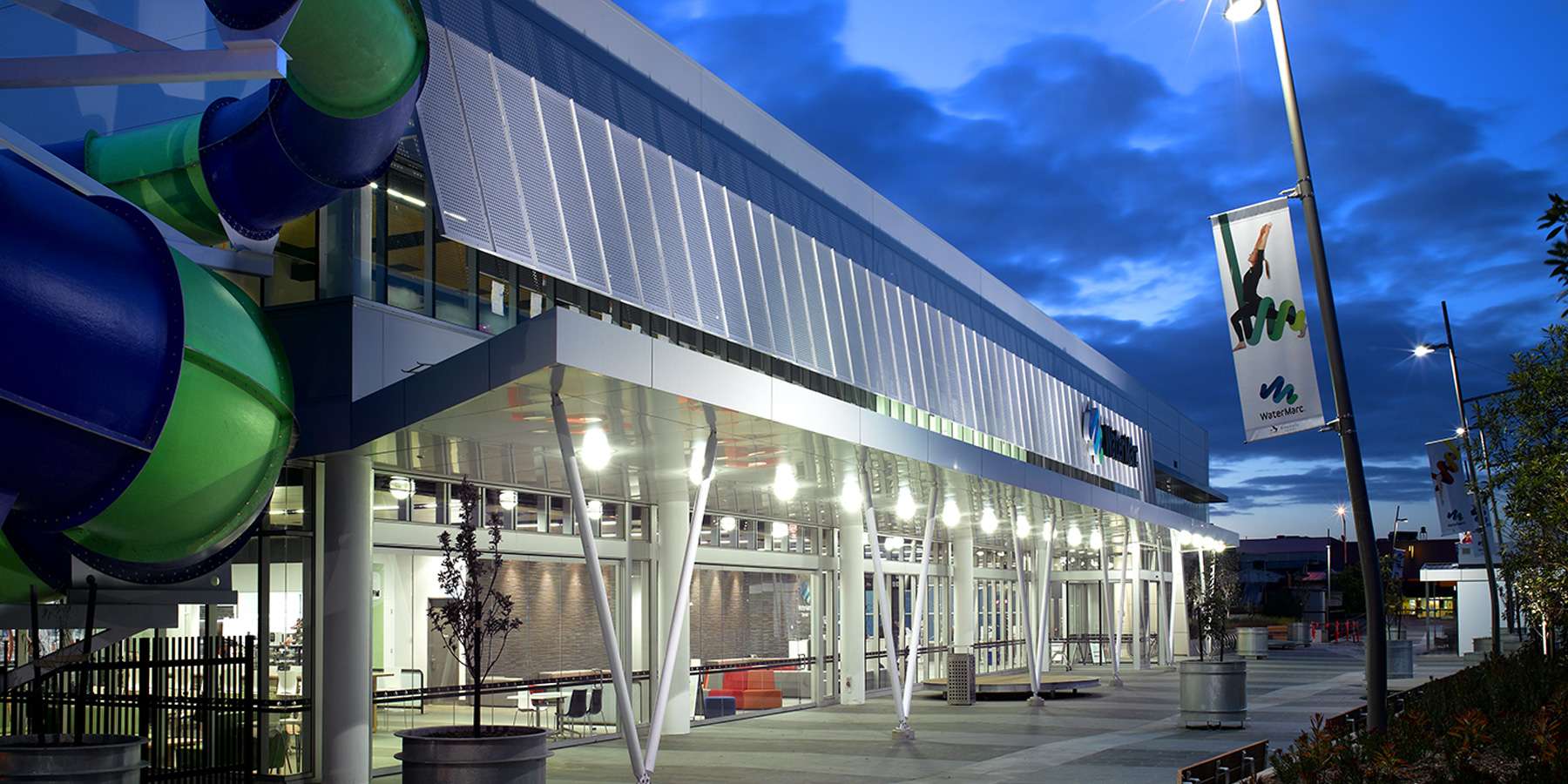 Modern building exterior illuminated at dusk, featuring large windows, sleek design, and colorful decorative elements.