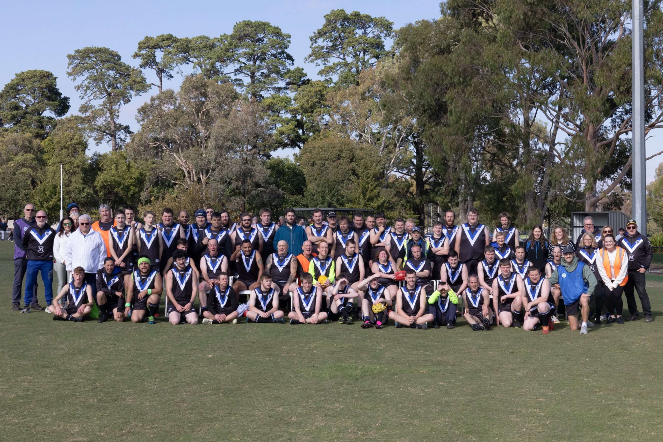 A team of people wearing navy jerseys with a white V shape on them smiling for the camera