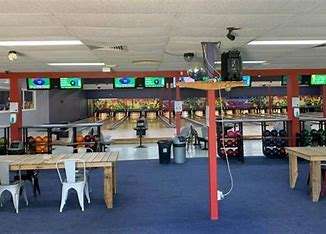 Interior of a bowling alley featuring colorful bowling lanes, seating areas with tables, and electronic scoreboards overhead.