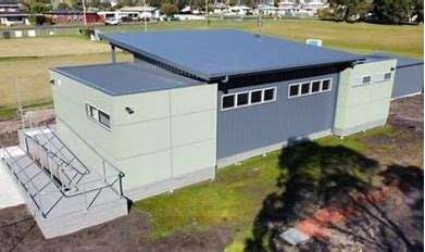 Image displays a grey and light green building with a green flat croquet ground in the background.