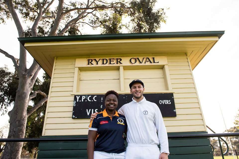 A female and male cricket player in front of the score board.