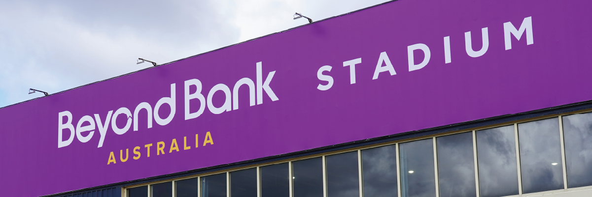 A large stadium with a large stadium sign with white text on bright pink background.