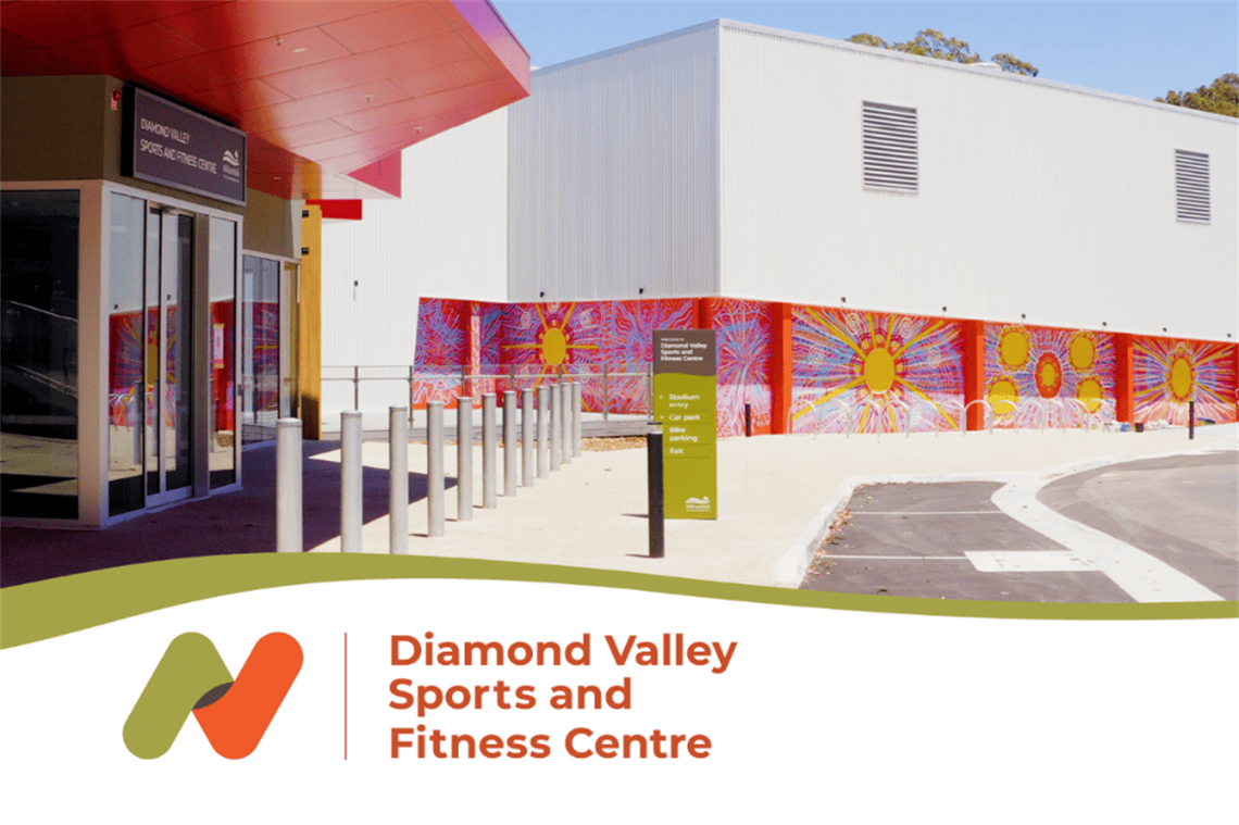 A large white stadium with red abstract roof surrounded by concrete paths and car park.