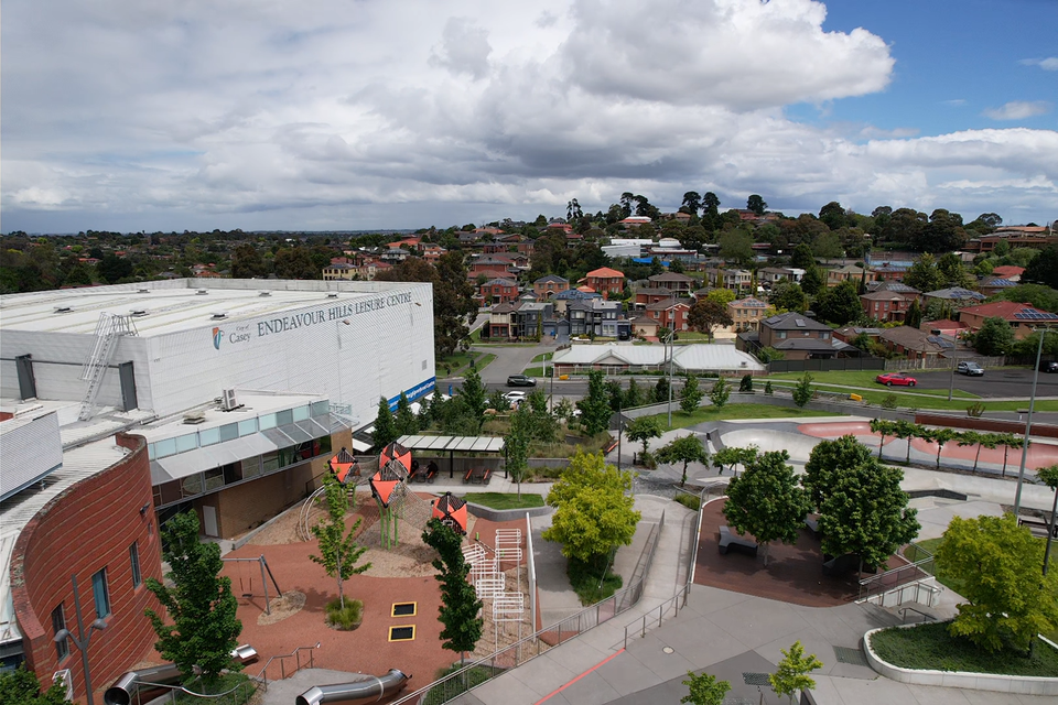 A large white stadium surrounded by concrete, roads and green trees.
