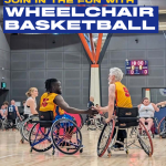 4 people playing wheelchair basketball - 2 players shaking hands wearing yellow vests