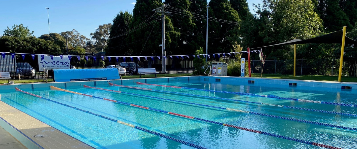 A large inground pool surrounded by green trees and grass.