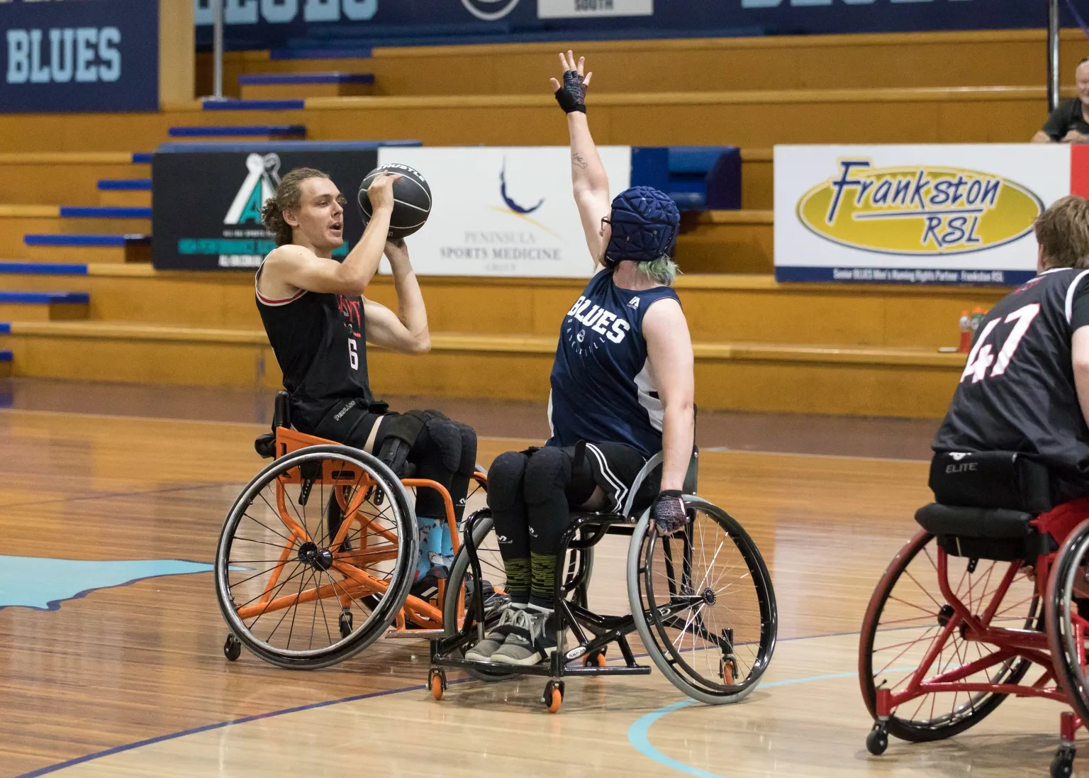 A male athlete in a wheelchair prepares to shoot a basketball, while a female opponent defends with her arm raised in a competitive match.